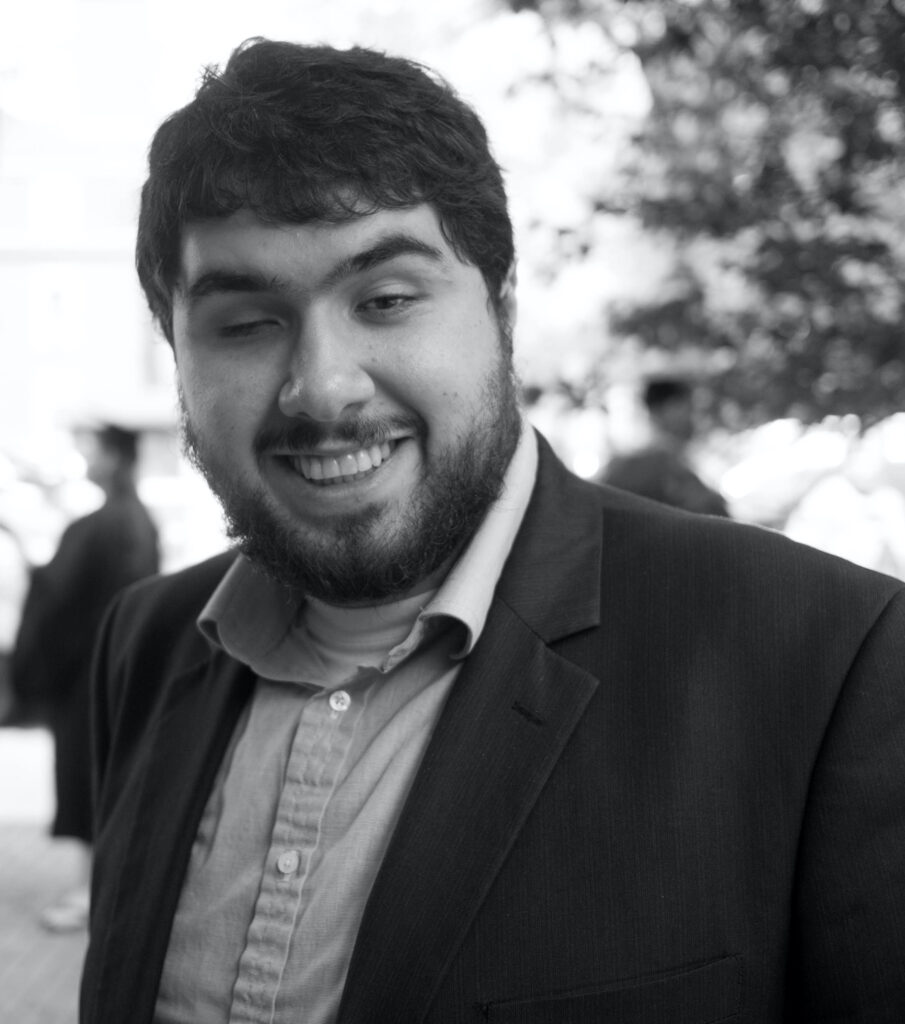 A black and white photo of Sina Bahram smiling and visible from mid chest up.